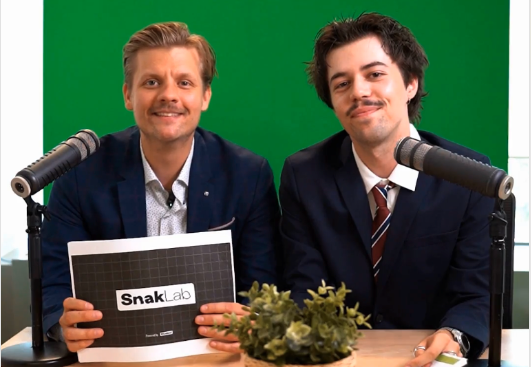 Deux présentateurs SnakLab en costume derrière des micros de podcast devant un fond vert, prêts à enregistrer SnakNews Q2.